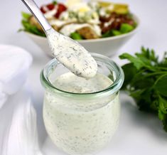 a salad dressing in a glass jar with a spoon sticking out of it next to a salad