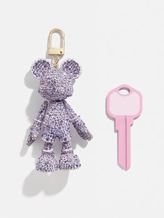 a keychain with a purple teddy bear on it next to a pink key