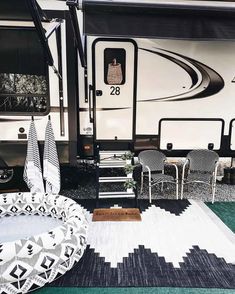 an rv is parked on the grass with chairs around it and a rug in front of it