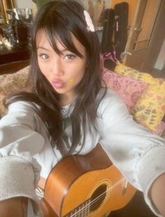 a young woman sitting on a couch holding an acoustic guitar in her hand and making a funny face