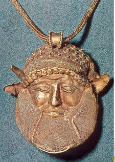 an old gold pendant with a face on it's side and a chain around the neck