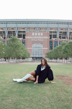 a woman is sitting on the grass in front of a large building and posing for a photo