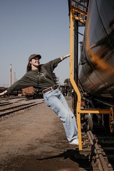 a man leaning on the side of a train with his arms out and one leg in the air