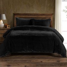 a bed with black comforter and pillows in a room next to a lamp on a dresser