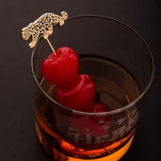 a glass filled with liquid and two red cherries on top of each other in front of a black background