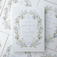 the wedding stationery is laid out on top of each other, with blue flowers and greenery