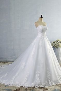 a white wedding dress is on display in front of a vase with flowers and a flower pot