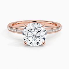 a rose gold engagement ring with diamonds on the band and a round cut diamond in the center