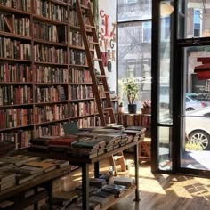 a bookshelf filled with lots of books in front of a window next to a wooden table