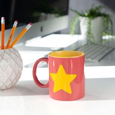 a pink mug with a yellow star on it next to a white cup filled with pencils