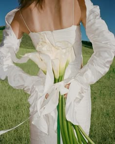 a woman in a white dress holding a bouquet of flowers with her hands behind her back