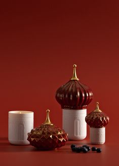 three red and white ceramic containers with gold trimmings sit on a red surface