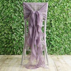 a chair with a purple bow on it sitting in front of a wall covered in greenery