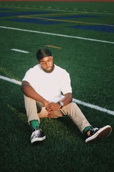 a man sitting on the ground in front of a football field with his hands together