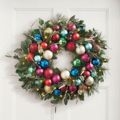 a christmas wreath hanging on the door with ornaments and greenery in front of it