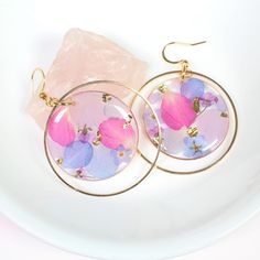 a pair of earrings with pink and blue flowers on them sitting on a white plate