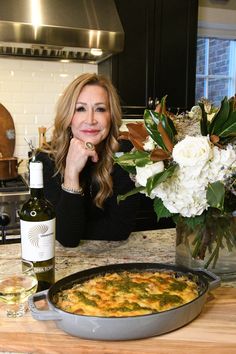 a woman sitting at a kitchen counter with a pot of food and bottle of wine