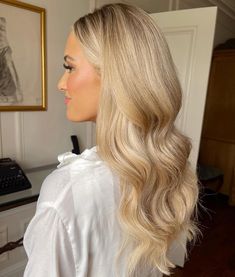 a woman with long blonde hair is standing in front of a desk and looking off into the distance