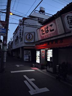 an empty street at night with signs on the buildings and power lines above it in japan