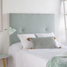 a bed with white linens and green headboard next to a ladder in a bedroom