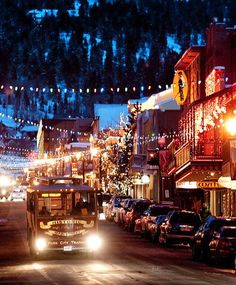 a city street at night with cars parked on the side and christmas lights strung across the buildings