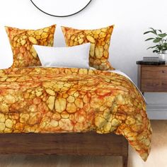 a bed with an orange and yellow comforter on top of it next to a clock