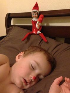 a young boy laying in bed next to an elf doll