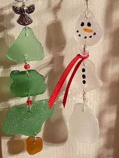 three snowman ornaments hanging from a white wall next to a red ribbon and green tree ornament