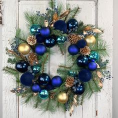 a wreath with blue and gold ornaments hanging on a white wooden door in front of a window