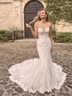 a woman in a wedding dress is standing on the cobblestone road and smiling