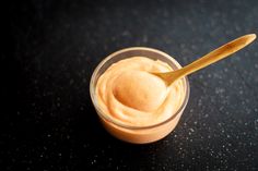 a wooden spoon is in a small glass jar filled with peanut butter on a black surface