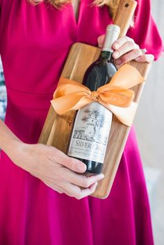 a woman in a pink dress holding a wooden tray with a bottle of wine on it