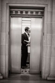 a man in a suit and tie standing at an elevator door with his hands on his hips