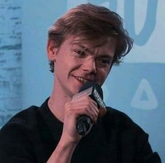 a man holding a microphone up to his face and smiling at the camera while wearing a black t - shirt