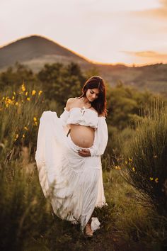 a pregnant woman in a white dress is walking through the grass with her hands on her belly