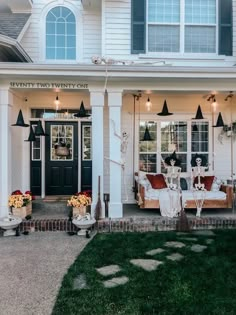 a white house with lots of windows and decorations on the front porch, along with potted plants