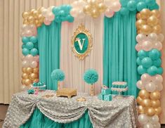 a table topped with balloons and cake next to a blue curtain filled with white and gold balloons