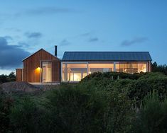 the house is lit up at night on top of a hill with trees and bushes