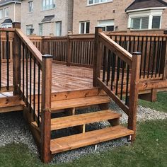 a wooden deck with steps and railings in front of a brick building on the grass