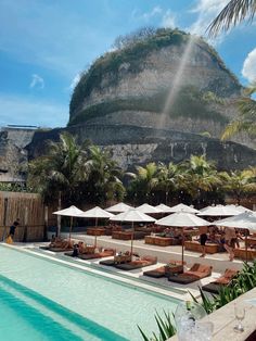 an outdoor pool with lounge chairs and umbrellas next to the mountains in the background