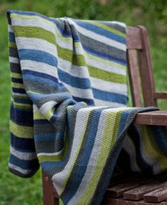 a striped blanket sitting on top of a wooden chair next to a grass covered field