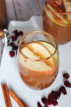 two glasses of apple cider with cinnamon sticks and cranberries on the side