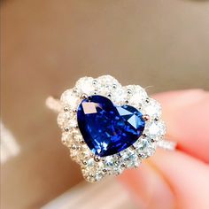 a blue and white heart shaped ring on someone's finger with diamonds around it