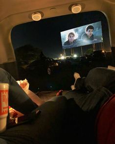 two people sitting in the back of a car watching a movie on a large screen