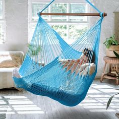 a woman laying in a blue hammock hanging from a wooden pole and looking out the window