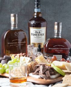 two bottles of old forester are sitting on a table with cheese, crackers and grapes