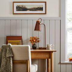 a desk with a lamp, chair and pictures on the wall in front of it