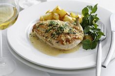 a white plate topped with meat and potatoes next to a glass of wine on a table