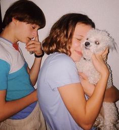 two young people are holding a white dog and kissing it's face on the cheek