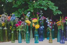 there are many different vases with flowers in them on the table outside, one is blue and the other is green